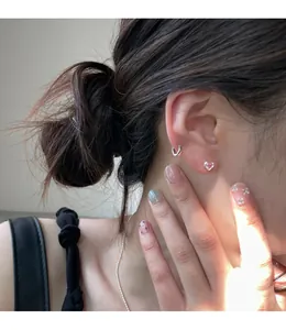 Close-up of heart-shaped pink zircon stud and silver hoop earring worn on the ear