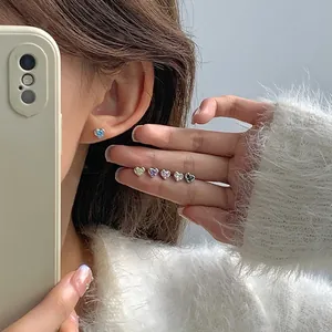 Silver heart stud earrings with colorful zircon stones shown on a model and in hand