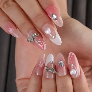 Detail of almond-shaped press-on nails with pink gradient, rhinestones and silver bows
