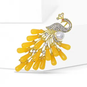 Elegant gold peacock brooch with white pearls and sparkling yellow gemstones on white background