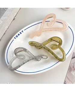 Three heart-shaped hair claws in pink, green, and grey on a white ceramic plate