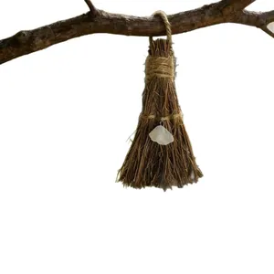 Handmade straw witch broom with white crystal heart pendant hanging on a branch