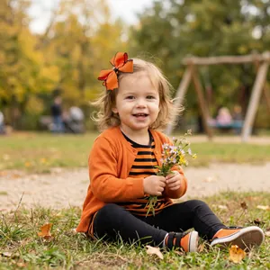 Kleinkind Mädchen mit orangefarbener Strickjacke und passender großer Haarschleife im Herbst