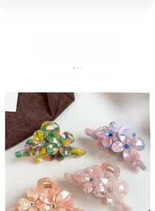 Détail d'une pince à cheveux florale en acétate avec strass sur un fond textile chaud