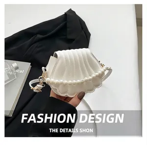 Detail der weißen Handtasche in Muschelform mit Kunstperlengriff und Steppmuster