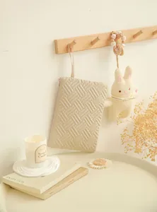 Quilted beige cosmetic bag with gold zipper hanging on a wooden hook in a cozy room