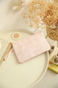 Detail of light pink quilted makeup bag with woven texture and a gold zipper