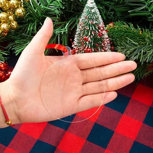 Close-up of clear acrylic Christmas ornament disc with red ribbon being held by hand