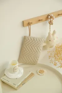 Close-up of beige quilted makeup bag with herringbone texture hanging on a wooden hook