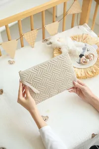 Close-up of beige quilted travel pouch held by hands in a cozy nursery setting