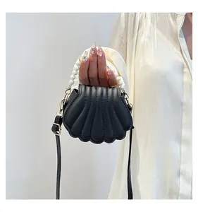 Détail du sac à main noir en forme de coquillage avec poignée perle et détails dorés