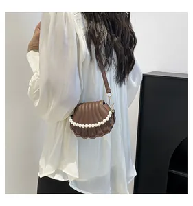 Détail d'un sac bandoulière marron en forme de coquille avec anse en perles dorées