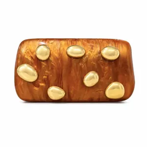 Detailed view of amber acrylic clutch with decorative golden pebble ornaments
