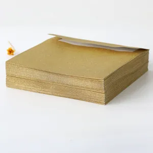 Close-up of stacked gold glitter square envelopes with a textured metallic finish