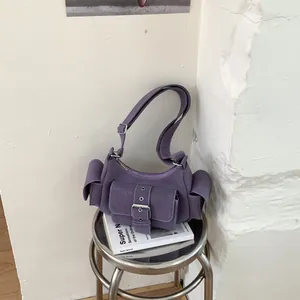 Detailed shot of purple suede underarm bag with multi-pocket design on white book