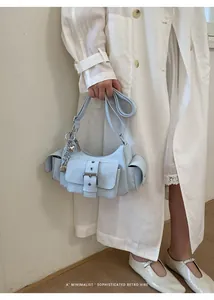 Detail of light blue leather crossbody bag with metal buckles and heart charm on model