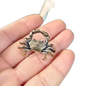 Detail of miniature vintage bronze crab ornament held by hand to show compact size