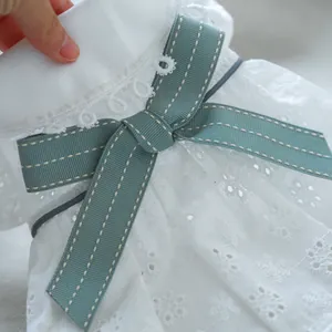 Detail of white eyelet lace dog shirt with floral embroidery and light green bow tie