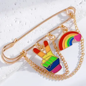 Detail of gold safety pin brooch with rainbow hand sign and heart charms on chain