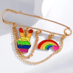 Detailed close-up of golden safety pin brooch with rainbow, V-sign charms and chains