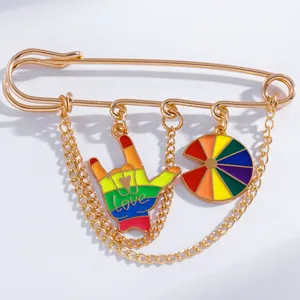 Detail of gold safety pin brooch with rainbow ILY gesture and rotating charm