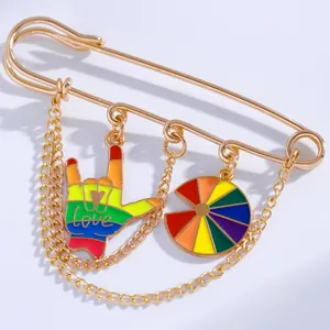 Detail of rainbow enamel hand and disc charms on a gold safety pin brooch with chain