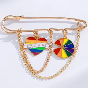 Macro detail of golden pin brooch with rainbow Love Wins heart and dangling chains