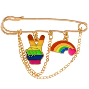 Detail of gold safety pin brooch with hanging rainbow heart and victory hand charms