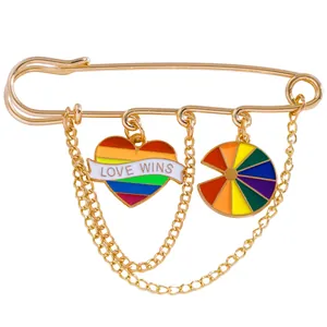 Macro detail of a gold safety pin brooch with rainbow Love Wins heart and dangling chains