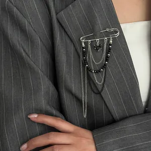 Detail of silver safety pin brooch with black heart pendant and layered chains on suit
