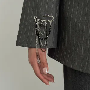 Detail of silver safety pin brooch with black beads and layered chains on suit sleeve