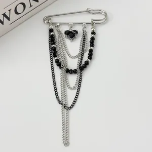 Detail of silver safety pin brooch with black heart gemstone and layered chains