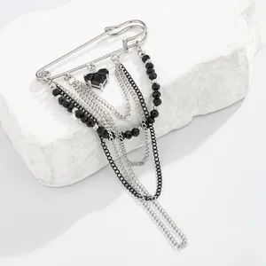 Macro detail of gothic silver safety pin brooch with black heart gem and layered tassels