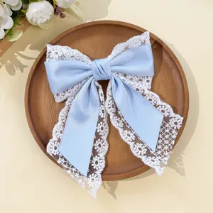 Detail of light blue satin bow hair clip with white lace trim on a wooden tray