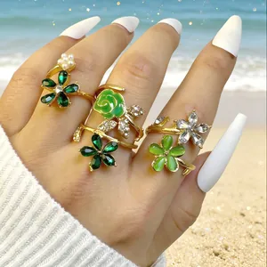 Detalle de cuatro anillos dorados florales con gemas verdes y perlas en la playa