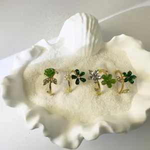Detalle de cuatro anillos florales dorados con rosas verdes y perlas en una concha