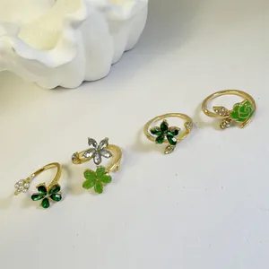 Vista detallada de anillos de flor dorados con strass verdes y perlas sobre concha