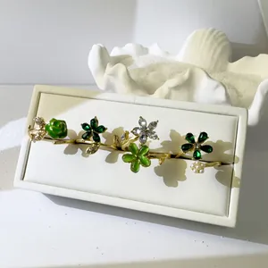 Detalle de anillos de flores y perlas doradas con esmalte verde en un soporte de joyas