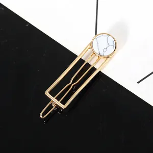 Detail of a hollow geometric gold hair clip with a round white marble pattern stone inlay