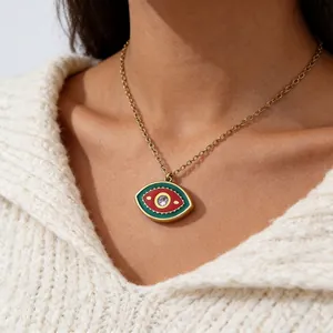 Close-up of gold evil eye pendant with green and red enamel worn on a female neck