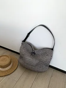 Detailed close-up of grey woven hollow straw bag with black faux leather strap and toggle