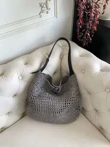 Close-up of a hollow woven straw shoulder bag with a black horn buckle and leather strap