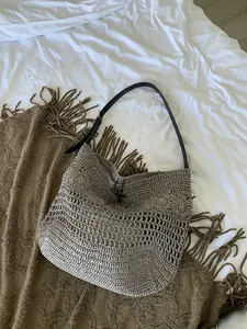 Close-up of hand-woven straw beach bag featuring a black horn toggle and leather strap