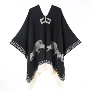 Detailed knit texture of poncho featuring wolf patterns and white fringe tassels