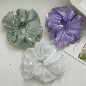 Detailed view of three satin scrunchies in mint, lilac, and cream with crystal beads