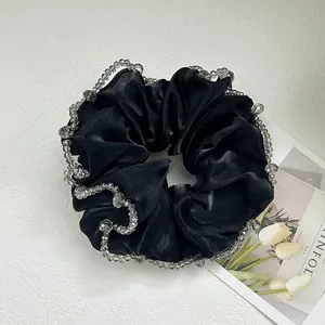 Detail of a black satin scrunchie featuring elegant grey crystal bead trim on fabric