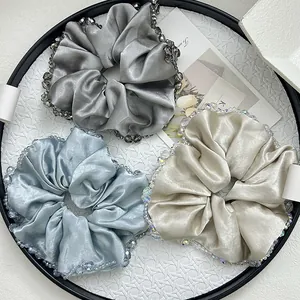 Detailed view of three satin hair scrunchies with crystal beads in grey blue and champagne