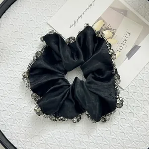 Detailed view of black satin scrunchie with grey beaded edges on a white tray
