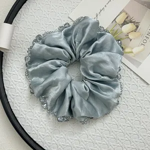 Close-up of light blue satin scrunchie with transparent crystal beads on a textured tray