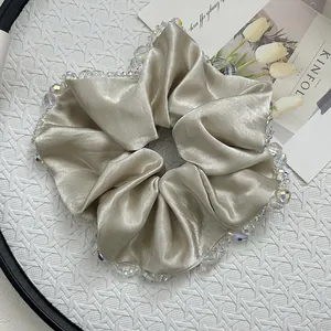 Close-up of champagne satin scrunchie featuring luxury crystal beads on white tray